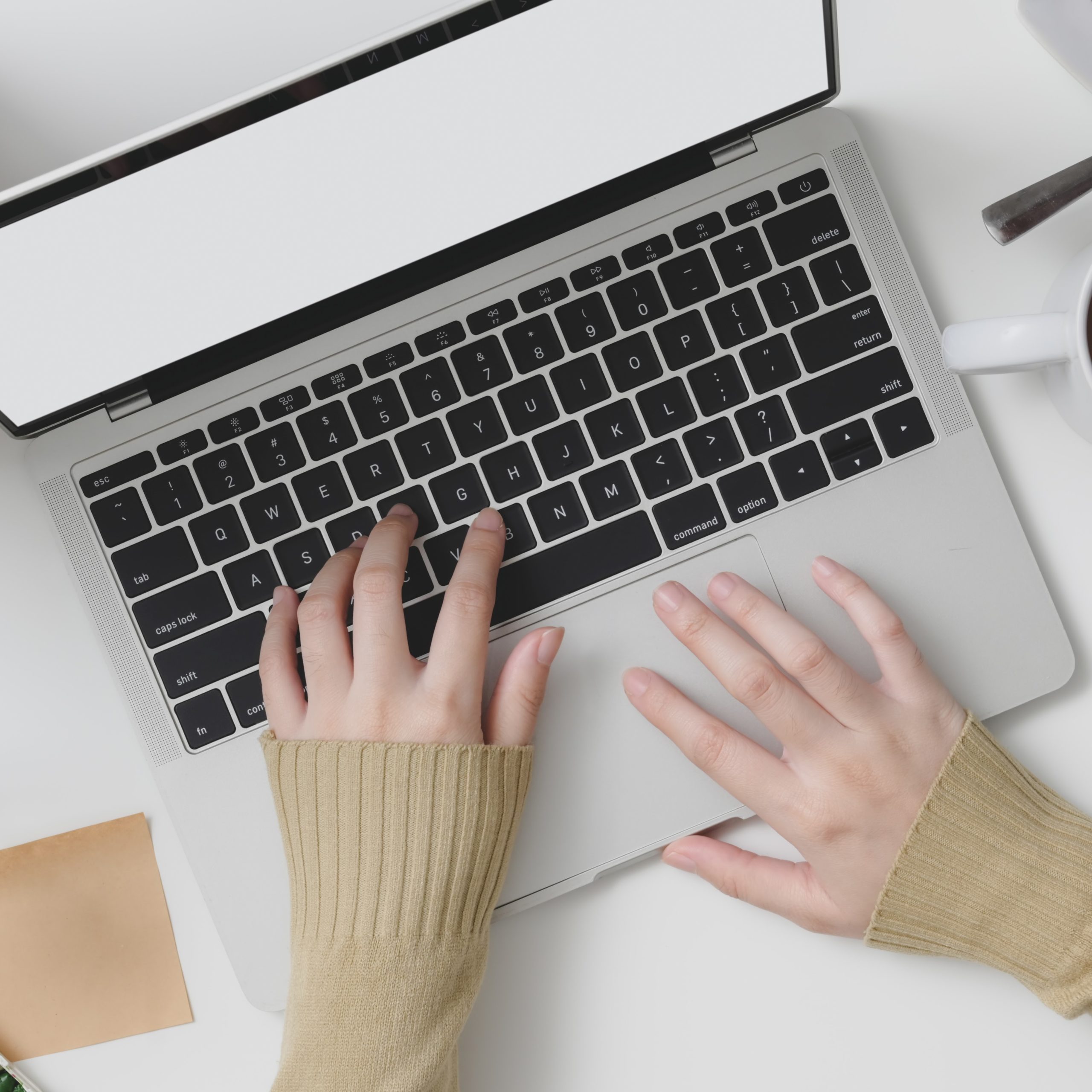 Top view of young female typing on laptop computer in cozy workspace with office supplies